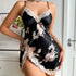 A model wearing black floral print satin slip dress with lace trim detail, posing against white wall with framed art