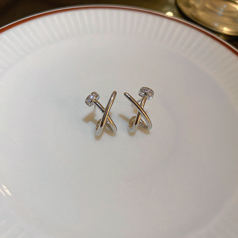 A pair of silver colored crossover hoop earrings with small embedded zirconia, displayed on a white ceramic plate.
