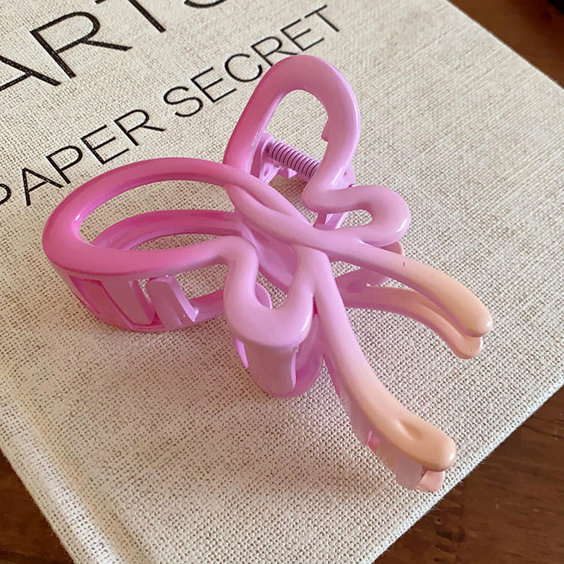 A pink butterfly-shaped hair claw with a soft gradient effect, placed on a fabric-covered book.