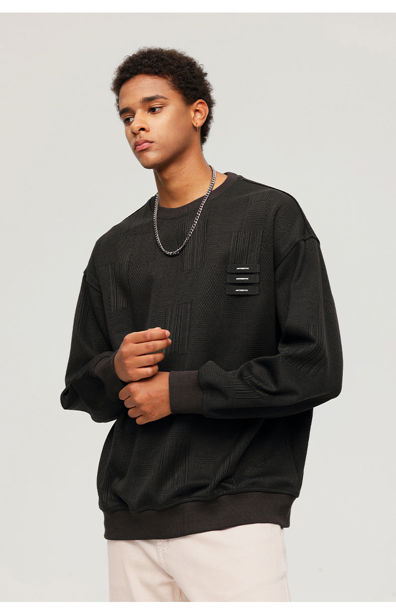 Side profile of male model wearing olive textured sweatshirt with decorative tabs and silver chain necklace