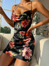 A model wearing black floral print satin slip dress with cowl neckline, sitting on white sofa with window view