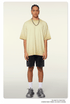 Model with braided hair wearing pale yellow ombre t-shirt with darker edges, silver chain necklace, black denim shorts and white socks