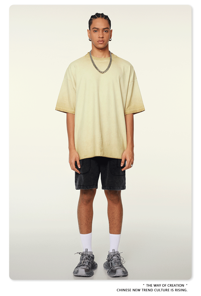 Model with braided hair wearing pale yellow ombre t-shirt with darker edges, silver chain necklace, black denim shorts and white socks