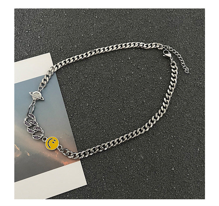 Full-length view of Cuban chain necklace laid flat on dark background, showcasing yellow smiley charm, planet charm, and crystal snake design