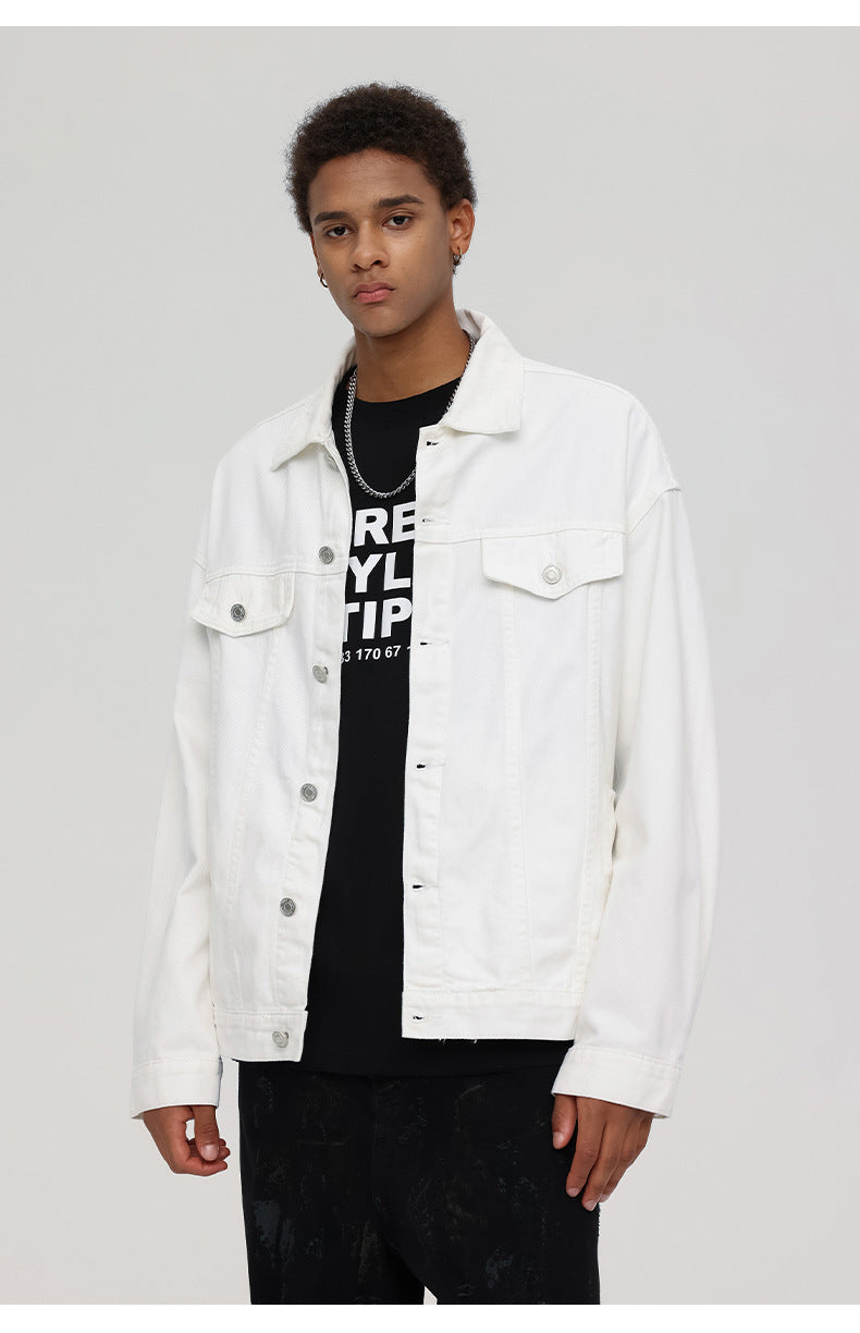 A man wearing white denim jacket over black graphic tee with silver chain necklace poses