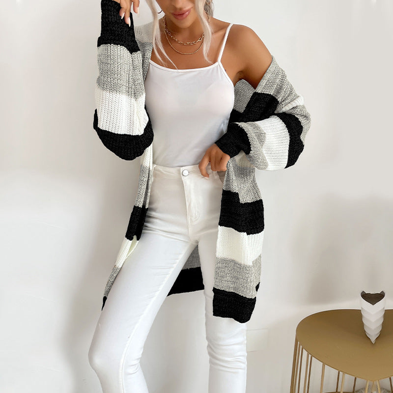 A woman in black, white and gray striped cardigan with white tank top and white jeans posing in modern minimal home setting