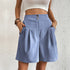 Powder blue pleated shorts with side pockets and decorative waistband buttons against white background