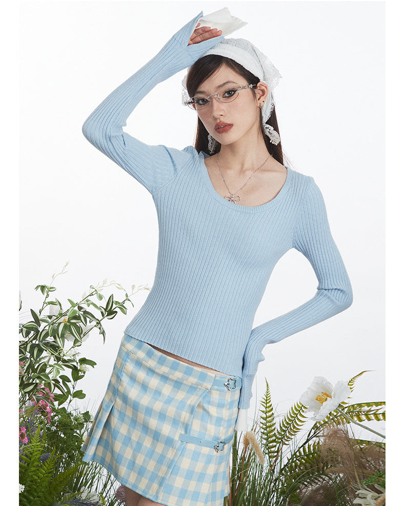 Close-up view of fitted ribbed sweater in powder blue with extended white cuffs, shown with coordinating gingham skirt featuring star embellishments