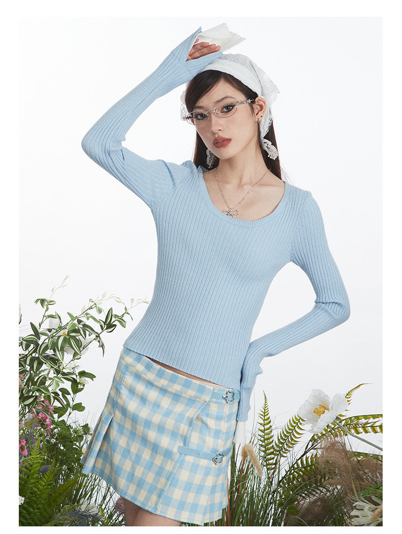 Close-up view of fitted ribbed sweater in powder blue with extended white cuffs, shown with coordinating gingham skirt featuring star embellishments