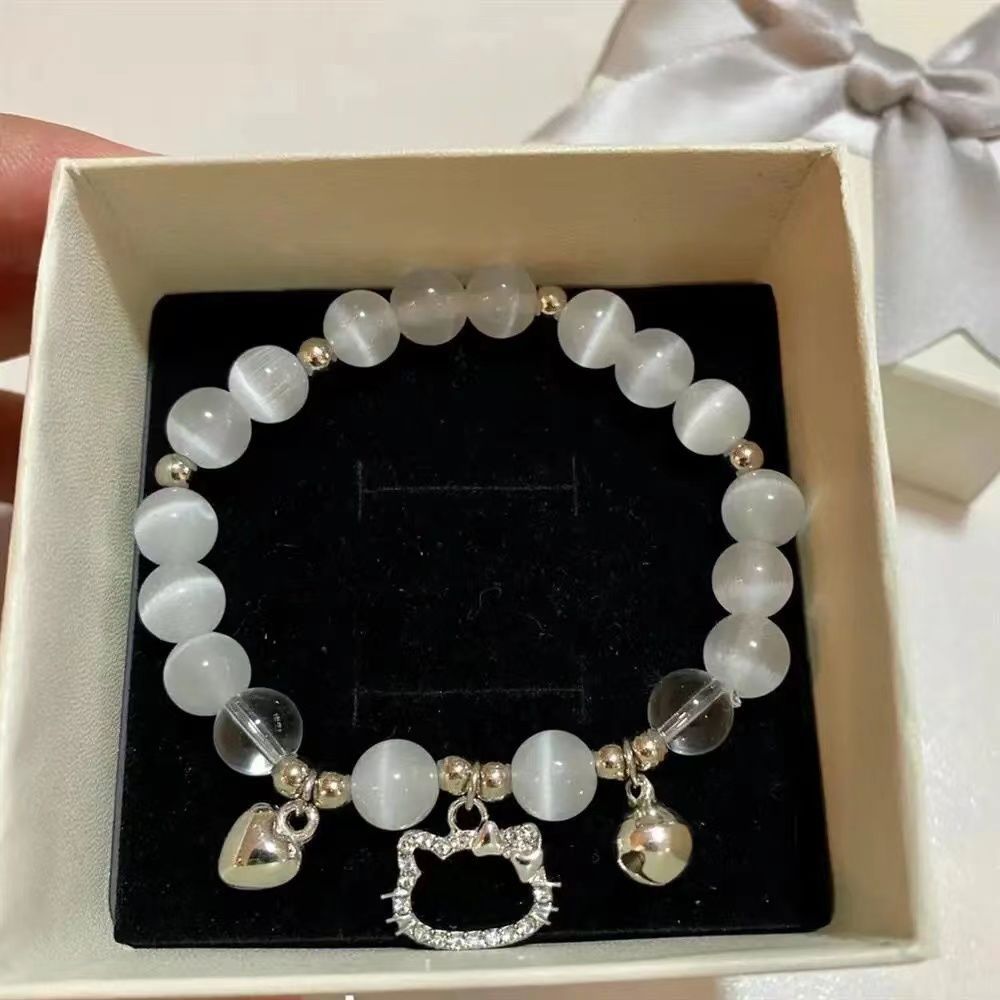 Cat-themed bracelet with white opal beads and silver charms including crystal cat face, heart, and bell, displayed in gift box