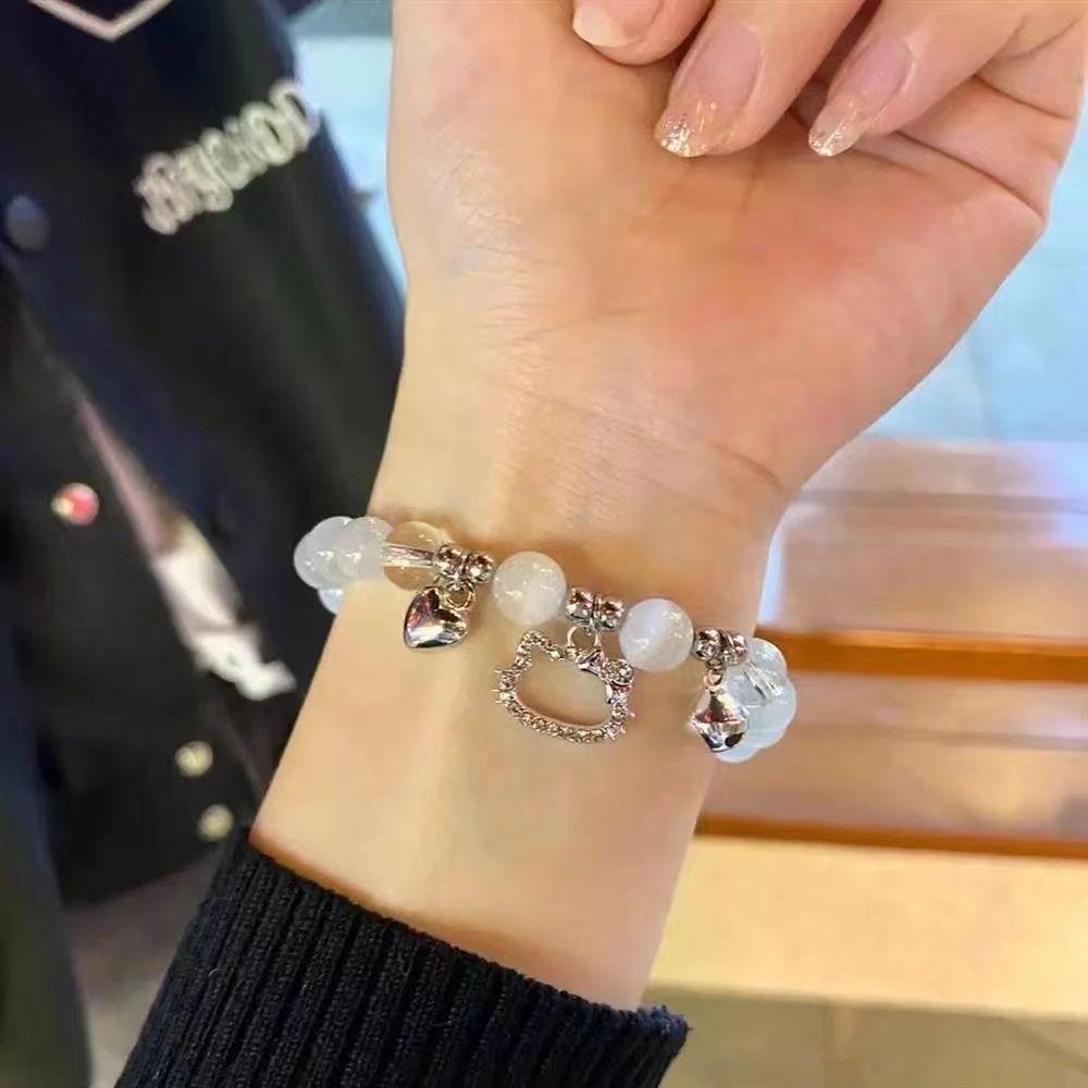 Cat charm bracelet with opal beads worn on wrist with black sleeve, showing glitter nail polish