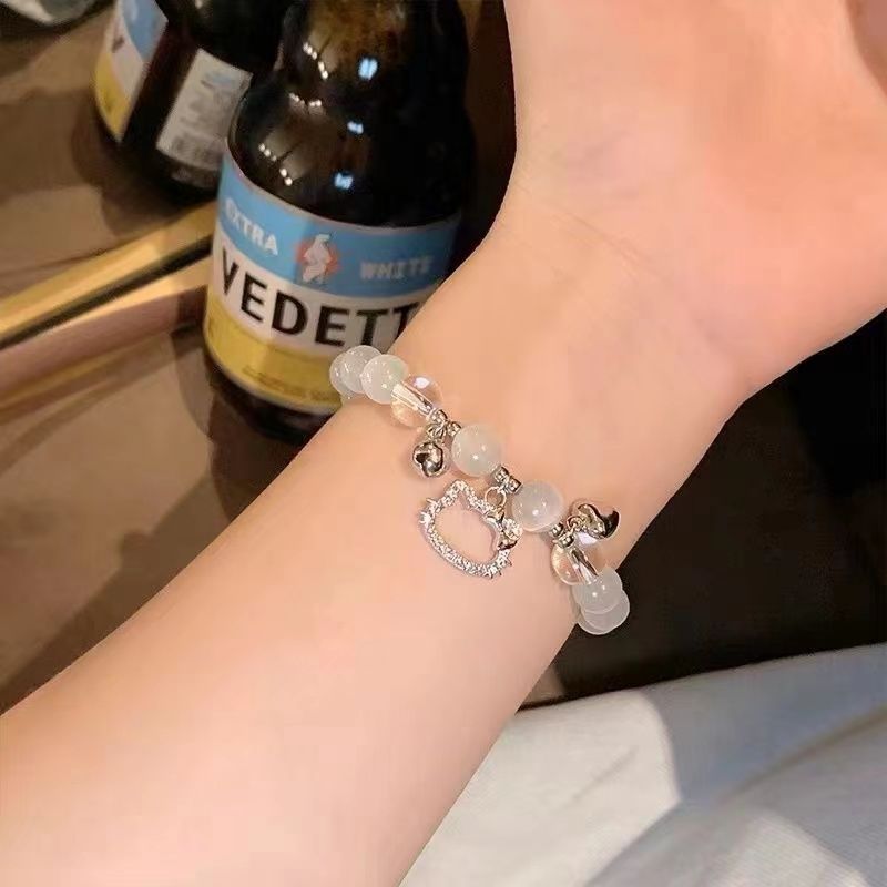 Opal bead bracelet with crystal cat charm and bells shown on wrist next to Vedett beer bottle