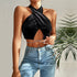 A model wearing a black velvet halter crop top with crossed front design, silver waist chain, and light blue jeans, styled with palm leaves backdrop