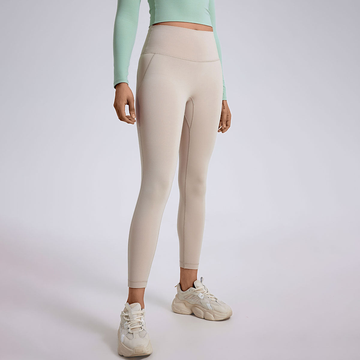 A model in cream colored high-waisted leggings with mint green crop top and matching cream sneakers, studio setting