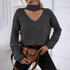 Woman wearing gray knit sweater with neck cutout, gold sleeve zippers, black jeans, and brown leather bag against white wall