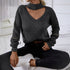 Woman sitting casually in gray knit sweater, black jeans and white sneakers, showing trendy neckline detail