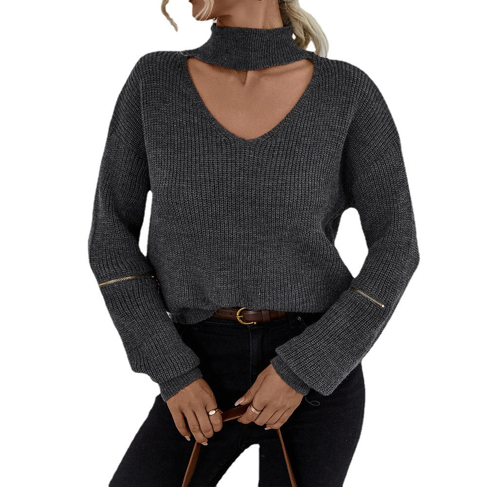 Woman in gray ribbed sweater with choker-style cutout, sleeve zippers, and dark jeans, holding brown leather purse