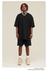Man wearing black oversized T-shirt and shorts set with silver chain and tan/beige Jordan sneakers