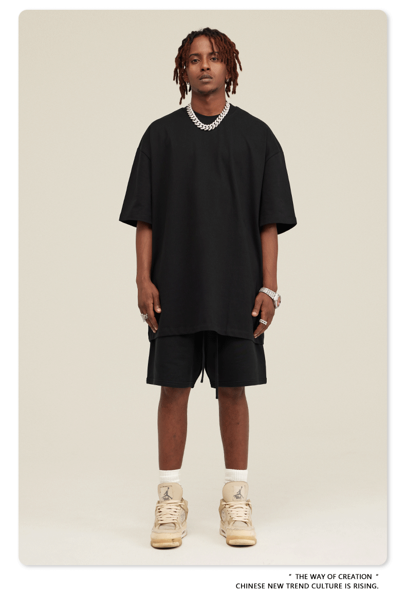 Man wearing black oversized T-shirt and shorts set with silver chain and tan/beige Jordan sneakers