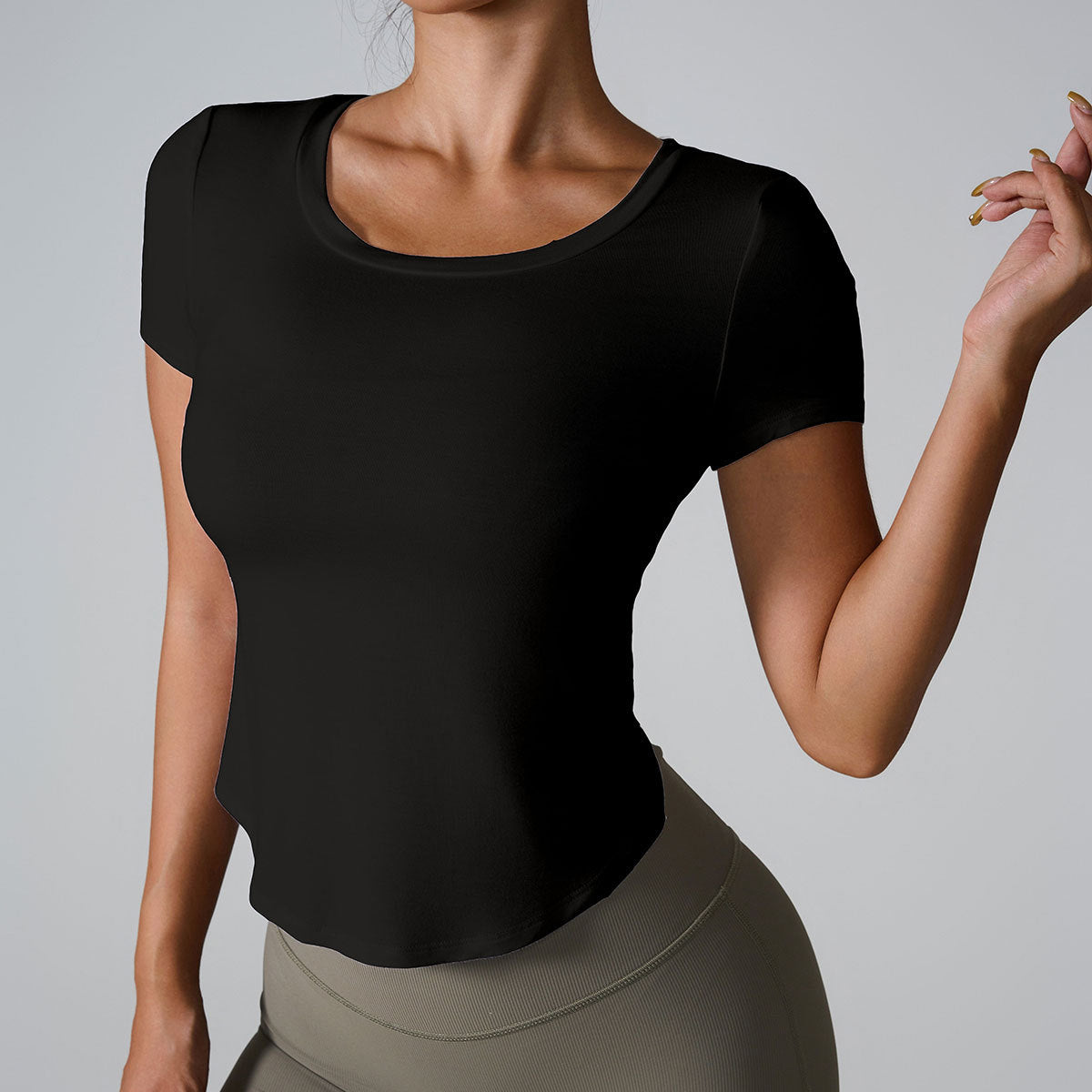 Woman in black fitted scoop neck t-shirt with curved hem paired with olive high-waisted leggings against gray background