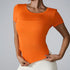 Woman wearing bright orange fitted t-shirt with scoop neckline paired with cream bottoms against light gray background
