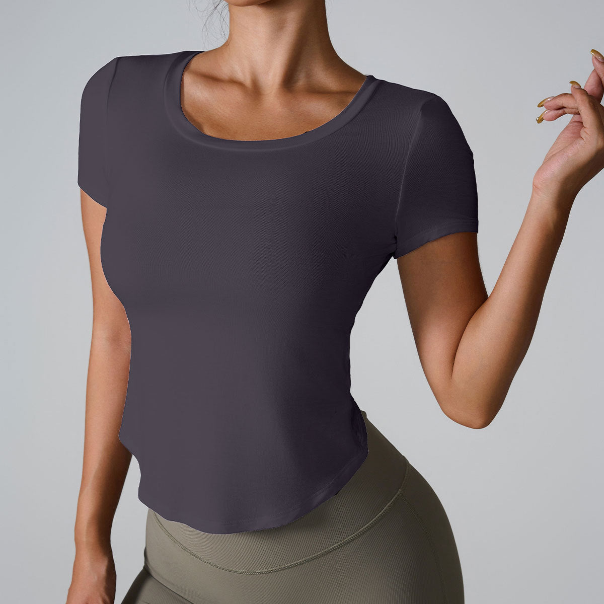 Woman wearing charcoal gray scoop neck t-shirt with curved hem paired with olive high-waisted leggings against gray backdrop