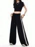 A woman is posing with hands in pockets wearing a two-piece black athletic set featuring a fitted crop top and flowy wide-leg track pants