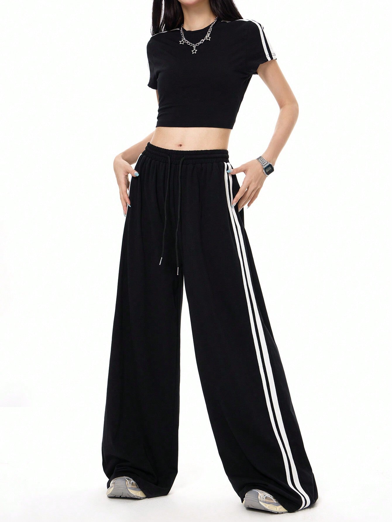 A woman is posing with hands in pockets wearing a two-piece black athletic set featuring a fitted crop top and flowy wide-leg track pants