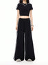 A woman is standing in a black athleisure two-piece set with white side stripes, featuring a crop top and wide-leg pants with drawstring waist