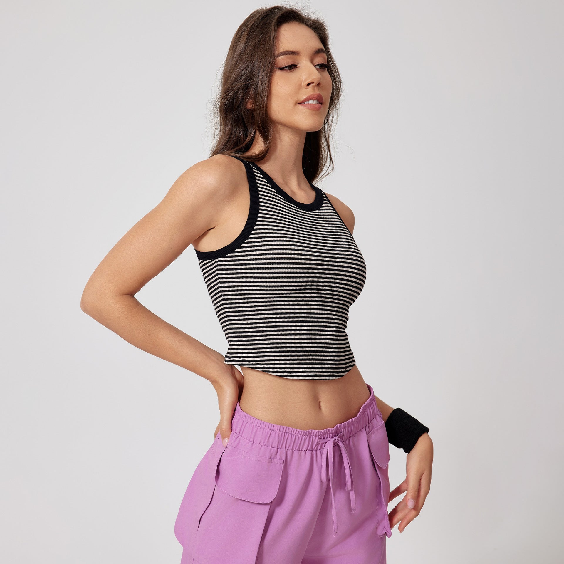 A woman in profile view wearing black and white striped crop tank with black trim and lilac cargo pants, styled against minimal white background