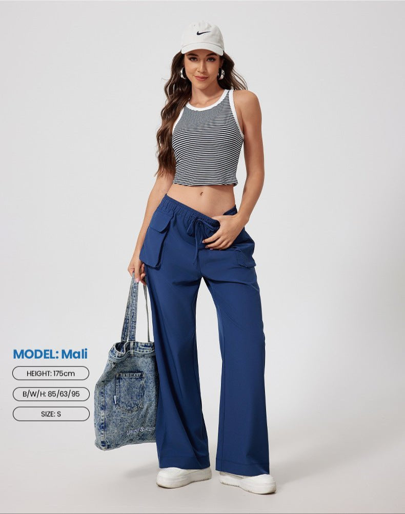 A woman modeling striped crop tank top with white trim and navy cargo pants, wearing Nike cap and holding denim tote, photographed against white backdrop