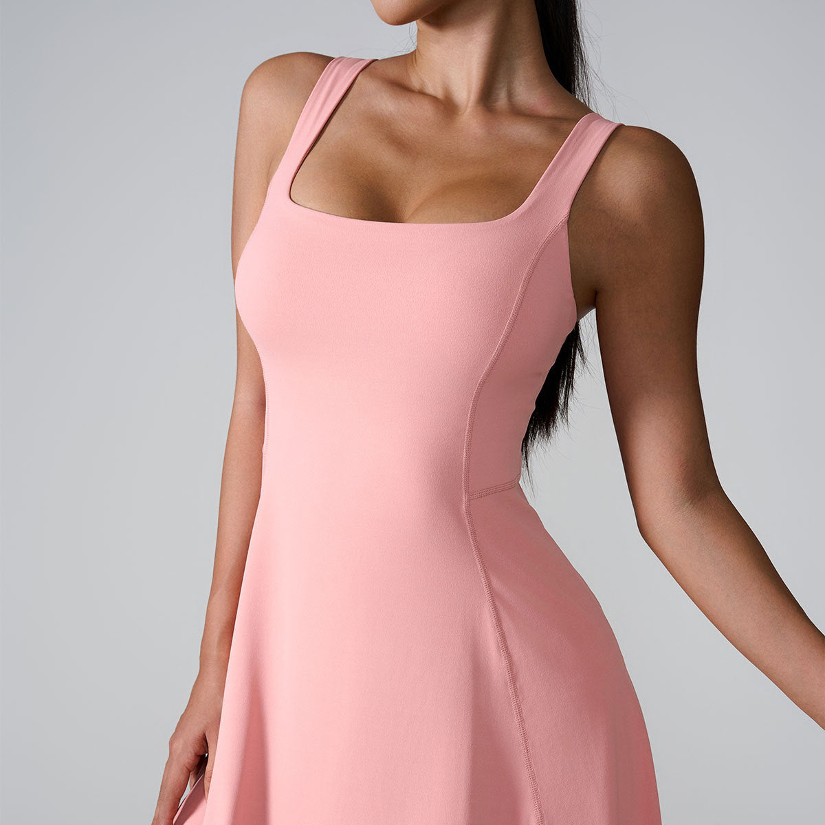 A model in blush pink sleeveless dress with square neckline and fitted bodice against neutral gray backdrop
