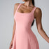 A model in blush pink sleeveless dress with square neckline and fitted bodice against neutral gray backdrop