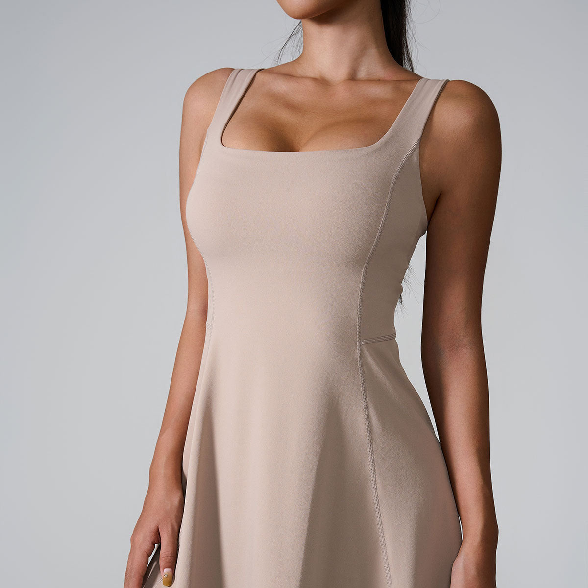 A model wearing nude square neck sleeveless dress with contoured seams and A-line silhouette against light gray background
