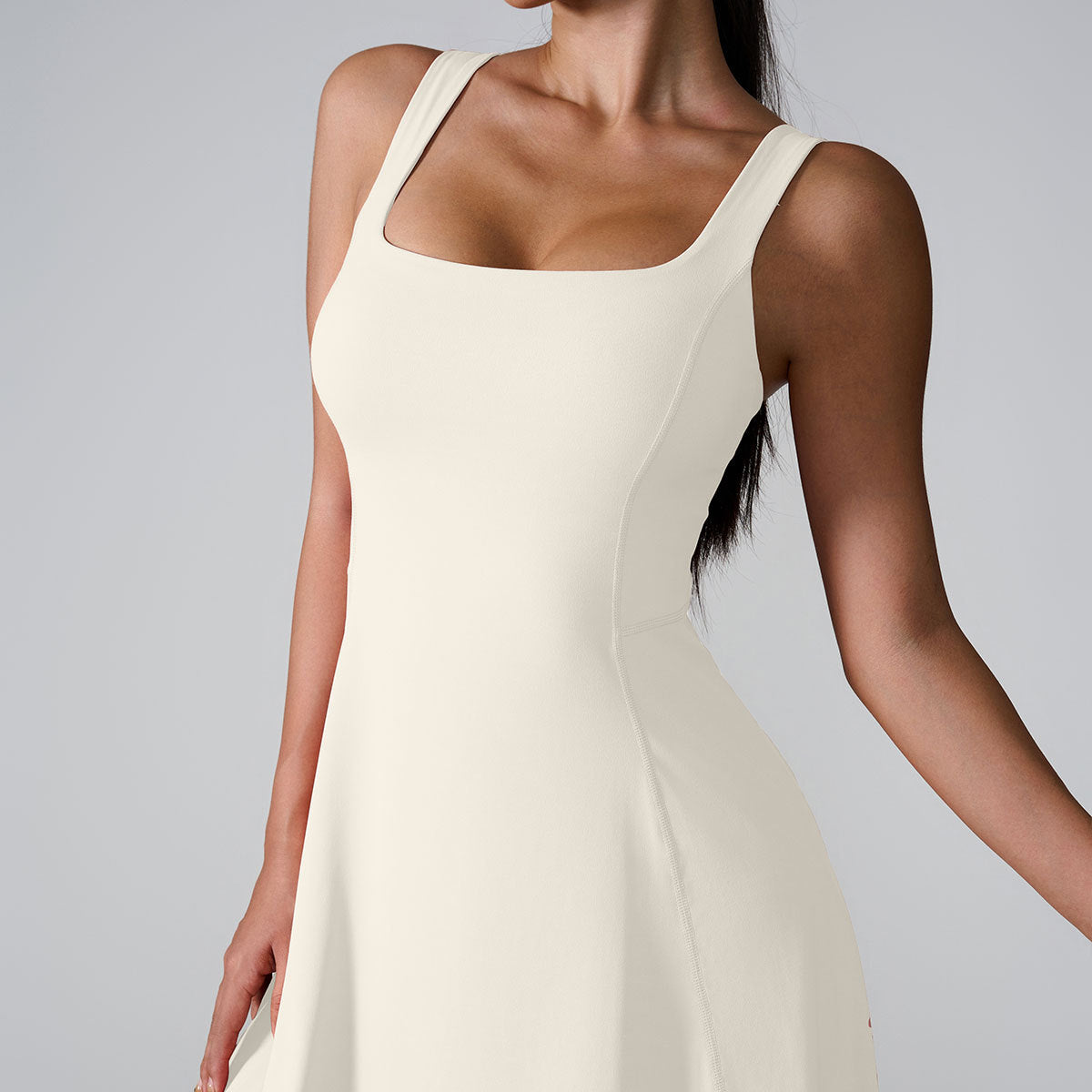 A model wearing ivory white square neck dress with wide straps and flared silhouette, photographed against light background