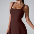 A model in chocolate brown square neck dress with structured fit and wide shoulder straps against light gray setting