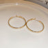Pair of polished gold hoop earrings with secure hinged closure displayed on white ceramic plate