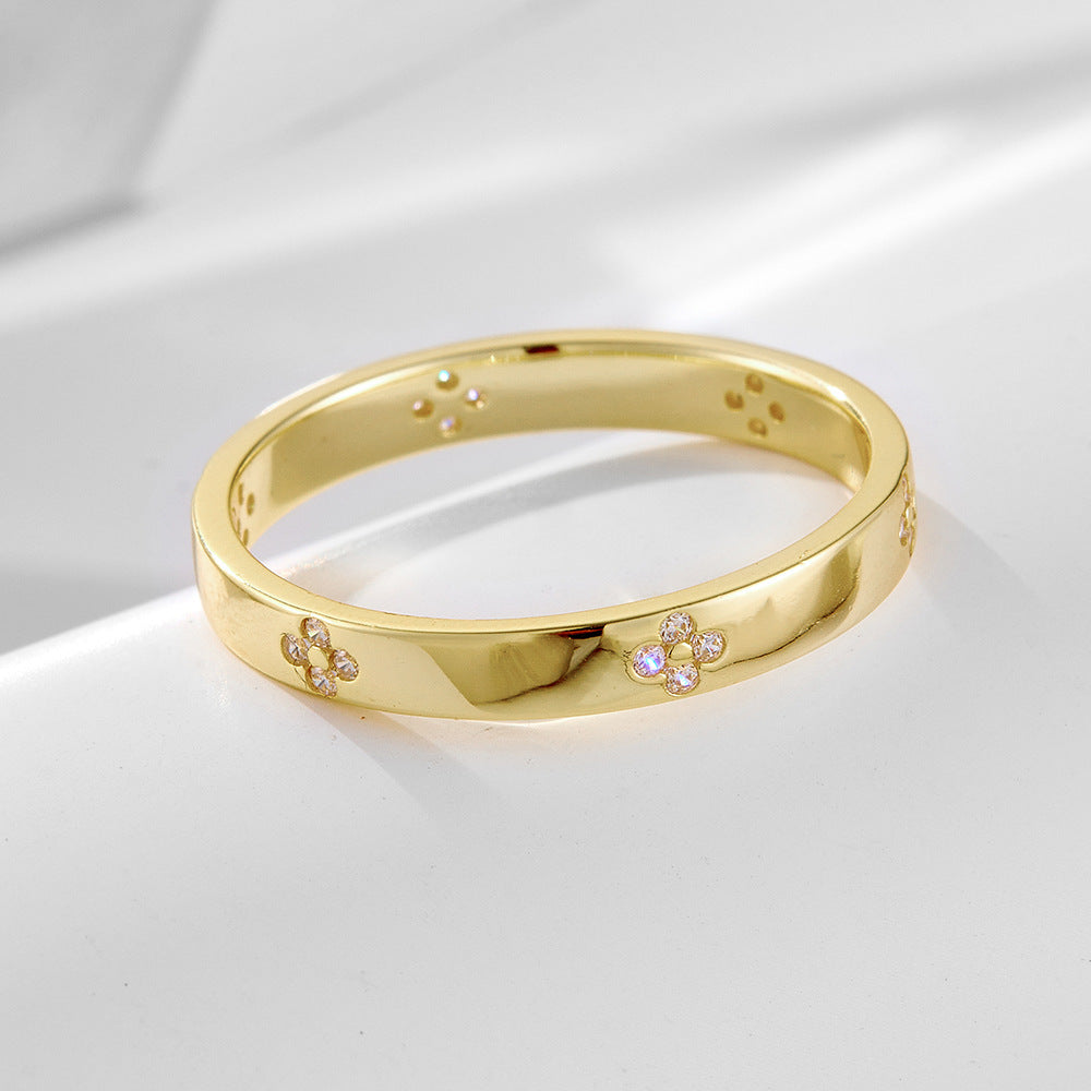 Gold wedding band with delicate flower-shaped diamond clusters arranged around polished band, displayed on white surface