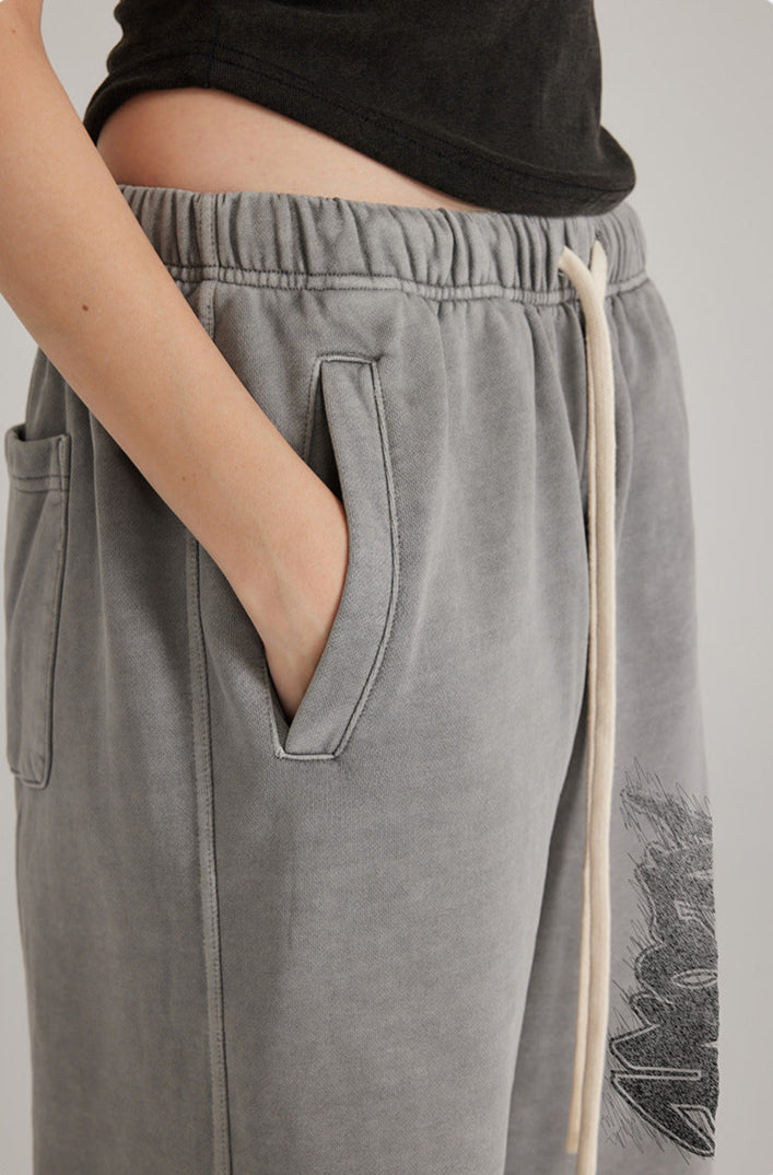 Close-up of grey sweatpants pocket detail showing elasticized waistband with white drawstring and streetwear-inspired design