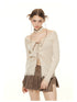 Close-up front view of cream ribbed sweater featuring off-shoulder neckline, lace-up front closure with distressed edges, styled with brown pleated mini skirt and cream studded choker.