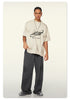 Front view of model in distressed white Beattube t-shirt and wide charcoal pants