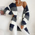 A woman wearing navy blue and white striped cardigan with white tank top and white jeans against clean white backdrop