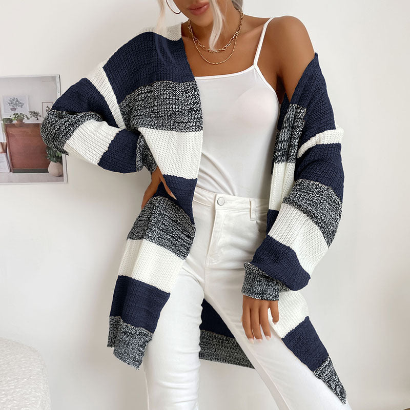 A woman wearing navy blue and white striped cardigan with white tank top and white jeans against clean white backdrop
