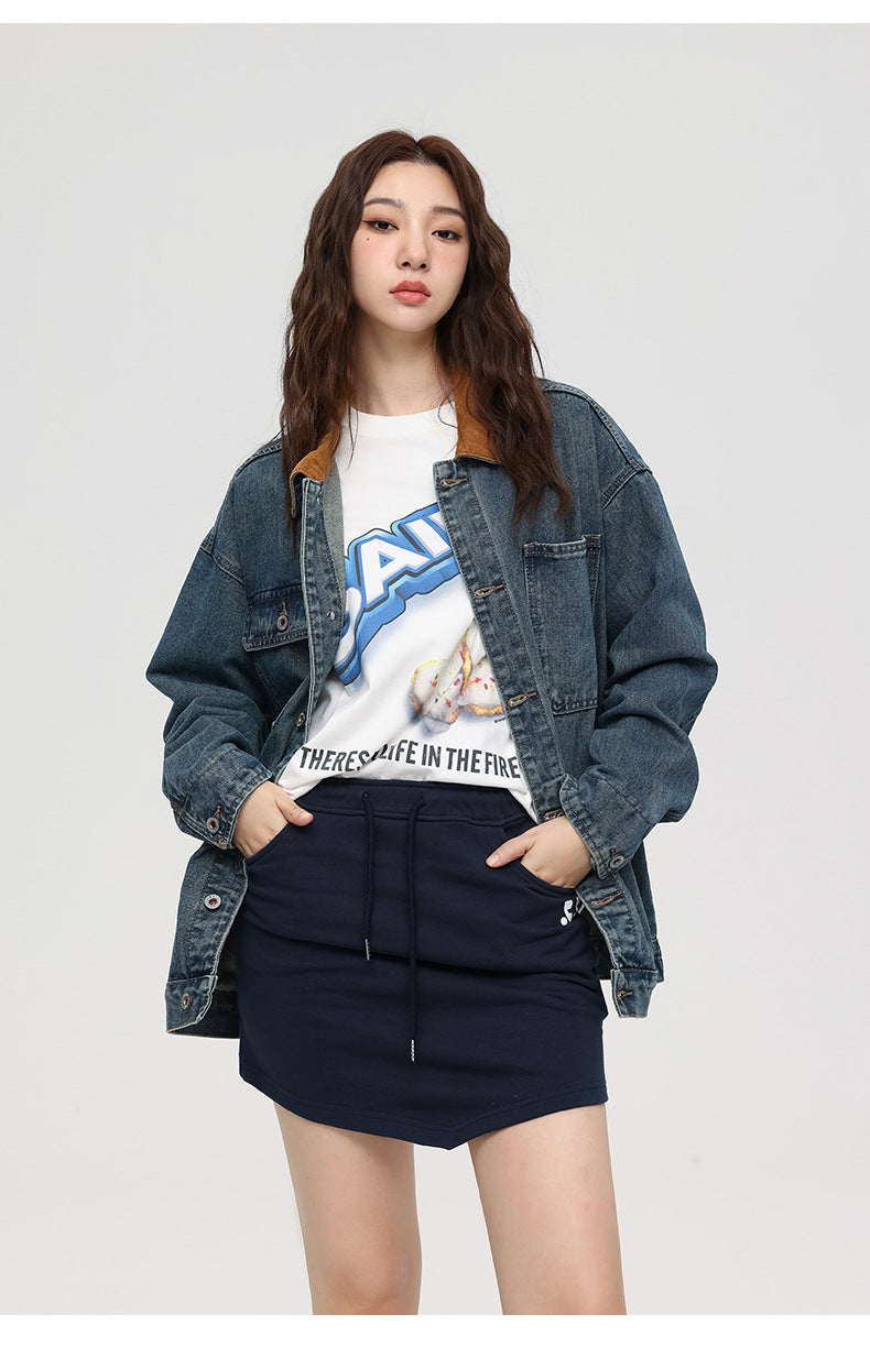 Woman in denim jacket with brown collar over graphic tee showing "LIFE IN THE FIRE" text and navy mini skirt