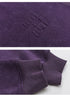 Close-up of purple sweatshirt embossed logo and ribbed sleeve cuff, showcasing texture and quality