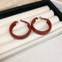 A jewelry display box with multiple pairs of gold and red hoop earrings, arranged in rows on a cushioned surface