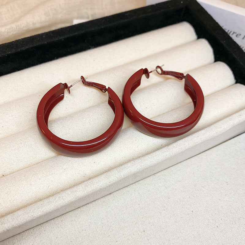 A jewelry display box with multiple pairs of gold and red hoop earrings, arranged in rows on a cushioned surface