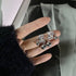 A hand holding silver dangle earrings with large clear gemstones and small metallic ball charms, against a dark background.
