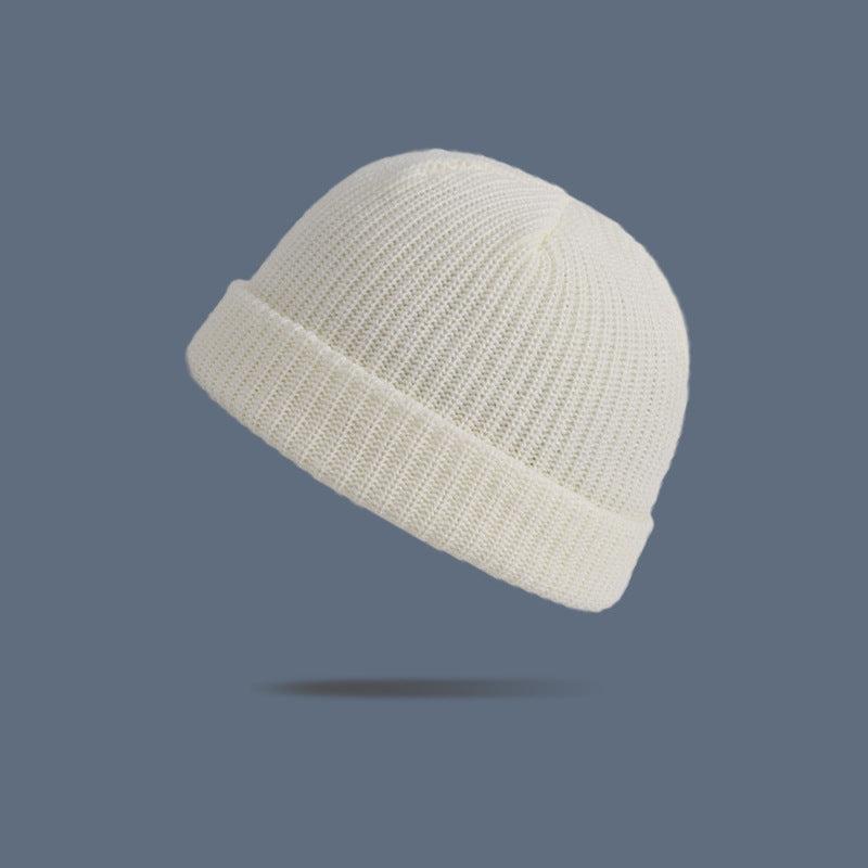 A cream white ribbed knit beanie with folded cuff floating against slate gray background, displaying versatile winter accessory