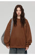 Close-up of woman with wavy brown hair wearing brown textured sweatshirt with three decorative tabs